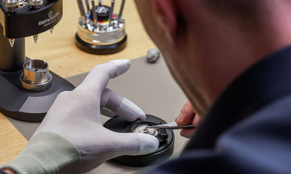 Das Bild zeigt den Uhrmachermeister bei dem Zusammenbau einer Automatikuhr. Hier wird das Uhrwerk in die Uhr eingesetzt. Anschließend erfolgt die Qualitätskontrolle.