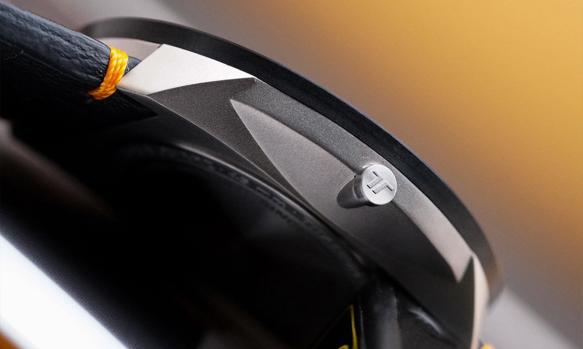 Detailaufnahme der BOTTA UNO 24 Jubiläumsedition Quarzuhr, die das markant gestaltete Titangehäuse mit der gravierten Krone zeigt. Die präzisen Kanten, die hochwertige Materialbearbeitung sowie das matte Finish unterstreichen den puristischen Designanspruch dieser preisgekrönten Designuhr. Das schwarze Lederarmband mit kontrastierenden orangefarbenen Nähten ergänzt das edle Erscheinungsbild dieser einzigartigen Einzeigeruhr – jetzt bestellen oder kaufen.