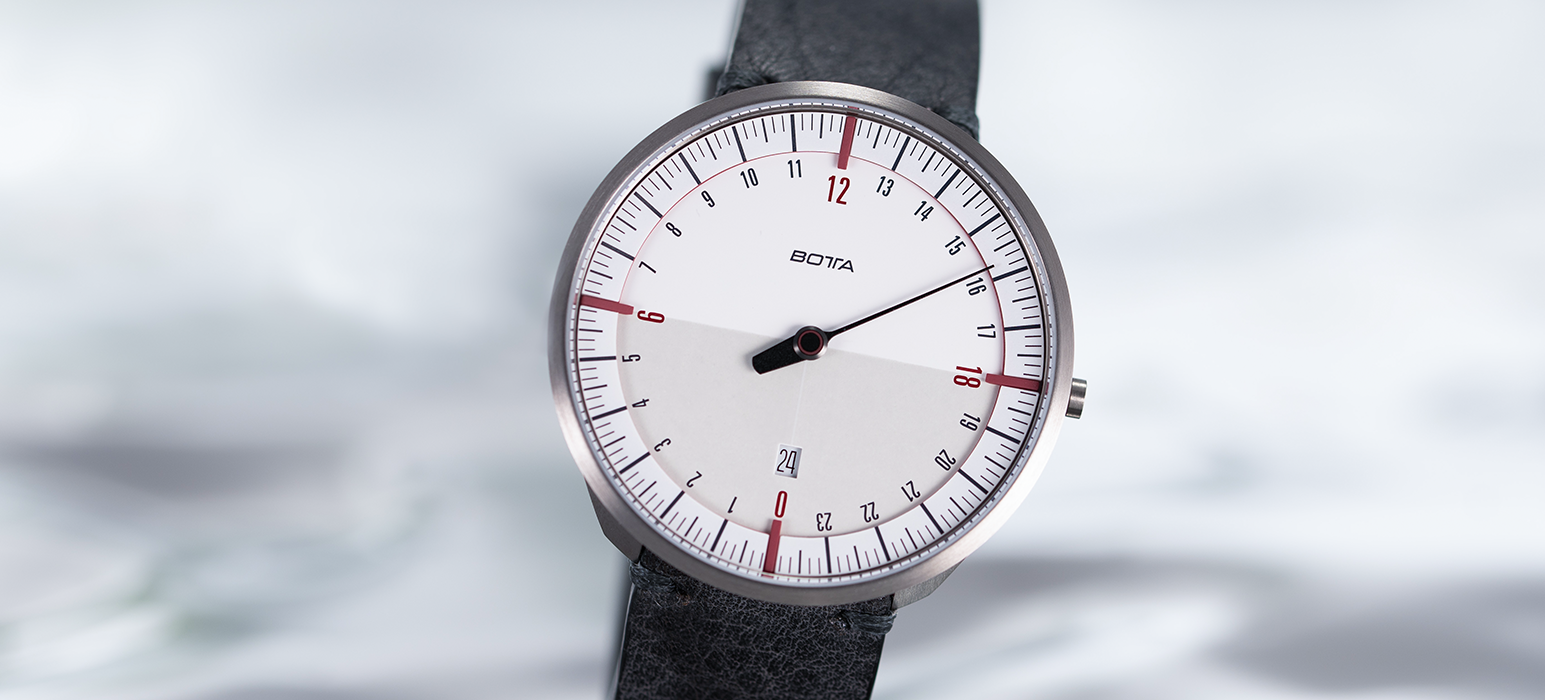 Die BOTTA UNO 24 Quarzuhr 45 mm mit weißem Zifferblatt und markanten bordeauxroten Markierungen bei 0, 6, 12 und 18 Uhr. Das 24-Stunden-Zifferblatt zeigt den Tagesverlauf in einem Blick, während der einzelne schwarze Zeiger die Zeit minimalistisch darstellt. Feine rote Akzente und das Datumsfenster bei 6 Uhr betonen die Designqualität. Eine preisgekrönte Designuhr für Puristen – exklusive Einzeigeruhr jetzt kaufen oder bestellen.