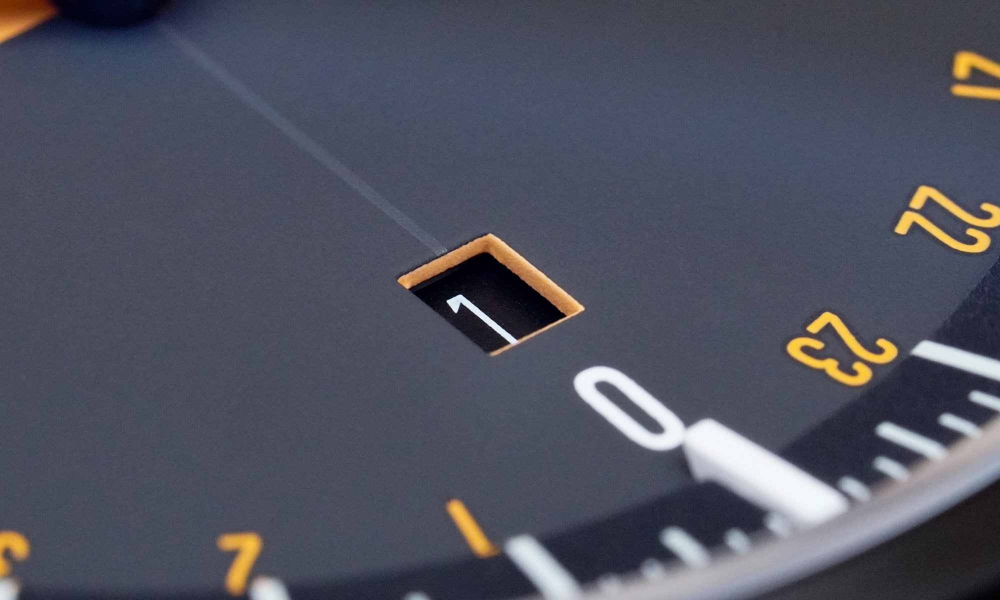 Detailaufnahme der BOTTA UNO 24 Jubiläumsedition Quarzuhr mit Fokus auf das Datumsfenster bei „0“. Das präzise eingearbeitete Quadrat zeigt die Zahl „1“ auf schwarzem Hintergrund, umrahmt von der warmen Farbgebung des Zifferblatts in Schwarz und Orange. Feine gelbe Stundenmarkierungen und die klare Typografie unterstreichen die hochwertige Verarbeitung dieser preisgekrönten Designuhr. Eine Einzeigeruhr für Liebhaber – jetzt kaufen oder bestellen.