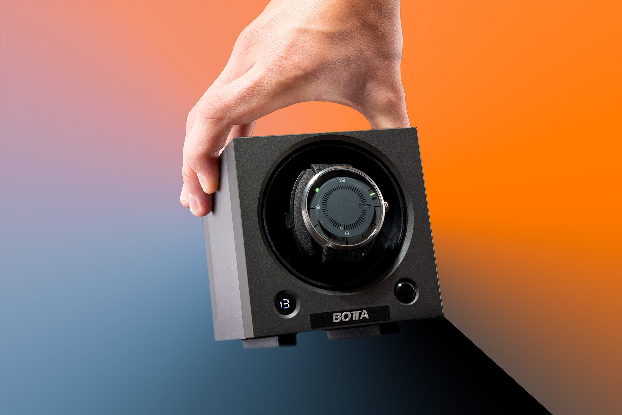 Ein BOTTA Uhrenbeweger im modernen, schwarzen Würfel-Design wird von einer Hand gehalten. Im Inneren rotiert eine BOTTA CLAVIUS Designuhr. Das Gerät verfügt über eine digitale Anzeige und hochwertige Verarbeitung. Der Uhrenbeweger für Designeruhren sorgt für konstante Bewegung von Automatikuhren und ist ideal für stilvolle Aufbewahrung und Pflege. Perfekt für Uhrensammler – jetzt kaufen oder bestellen.