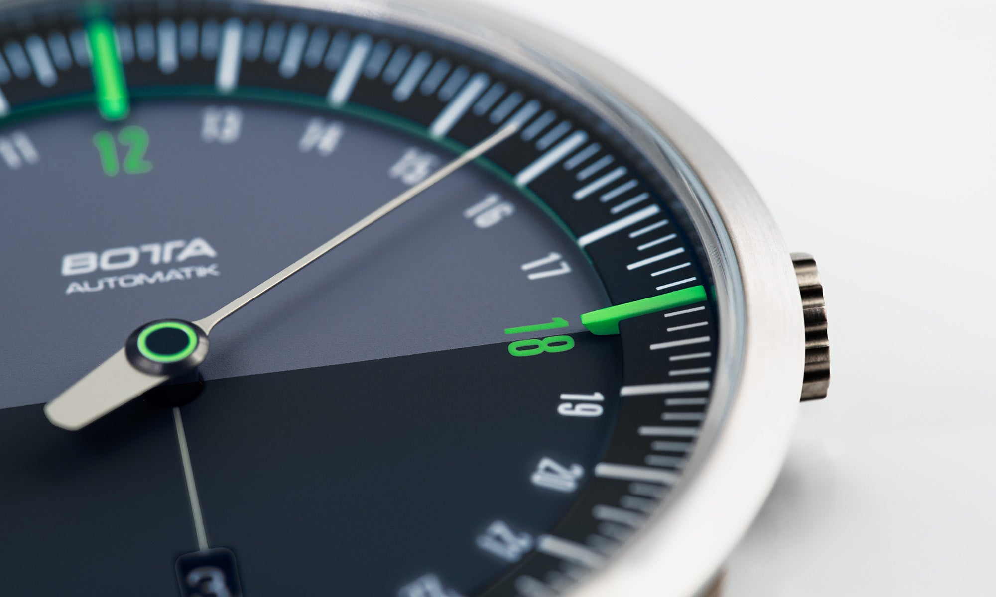 Detailaufnahme der BOTTA UNO 24 Automatik: Zu sehen ist das schwarze 24-Stunden-Zifferblatt mit grün hervorgehobenen Markierungen und einem einzigen Zeiger. Diese Automatikuhr stellt den gesamten Tagesverlauf in einer Umdrehung dar und verbindet klares Design mit Logik. Das Tri-Titan-Gehäuse und das Sellita SW330 Automatikwerk machen diese Einzeigeruhr zu einer hochwertigen Designuhr. Eine besondere Armbanduhr für alle, die eine Uhr mit einem Zeiger kaufen oder bestellen möchten.