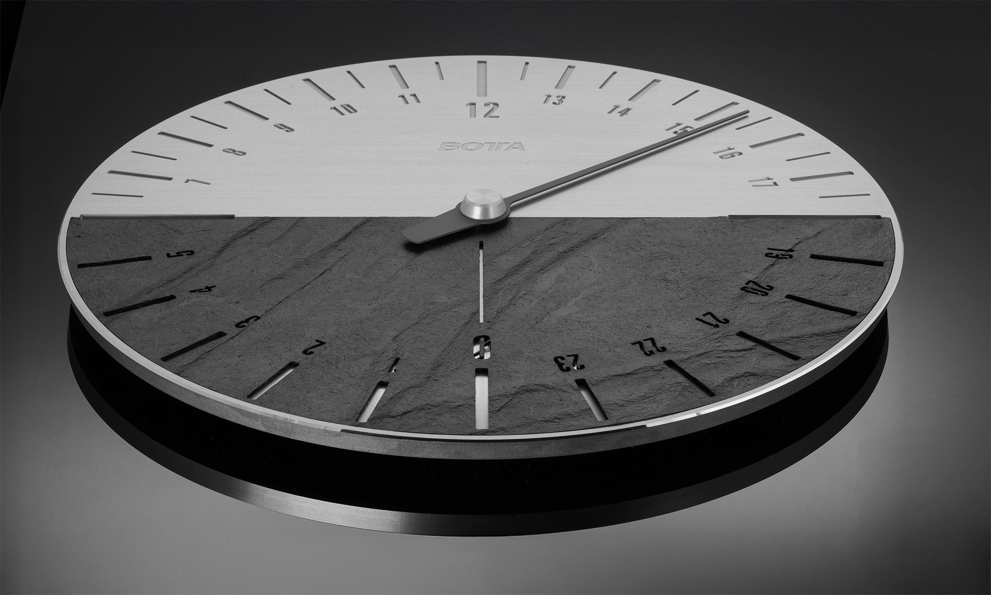 Die UNO 24 Slate Designwanduhr vereint Naturmaterial und Technik: Das Bild zeigt das Zifferblatt mit halbierter Tag-Nacht-Darstellung, wobei die obere Hälfte in gebürstetem Metall und die untere in echtem Schiefer gehalten ist. Ein einziger Zeiger durchläuft in 24 Stunden den Kreis – typisch für die 24-Stunden Wanduhr im Schieferdesign. Eine stilvolle Designwanduhr für bewusste Zeitwahrnehmung. Jetzt kaufen oder bestellen