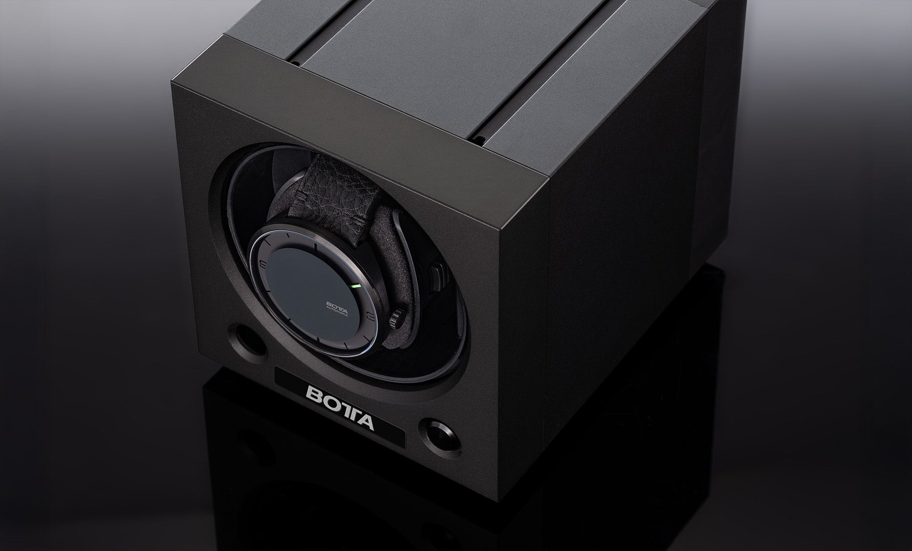 Eleganter BOTTA Uhrenbeweger in mattschwarzem Gehäuse, hier mit einer eingelegten Designeruhr sichtbar durch die runde Frontöffnung. Das minimalistische Design aus Aluminium verbindet Funktion und Ästhetik und sorgt für die kontinuierliche Bewegung von Automatikuhren. Die kompakte Uhrenbox schützt vor Stillstand und unterstreicht den modernen Lifestyle anspruchsvoller Uhrenträger. Ideal zum Kaufen oder Bestellen für Designuhr-Besitzer.