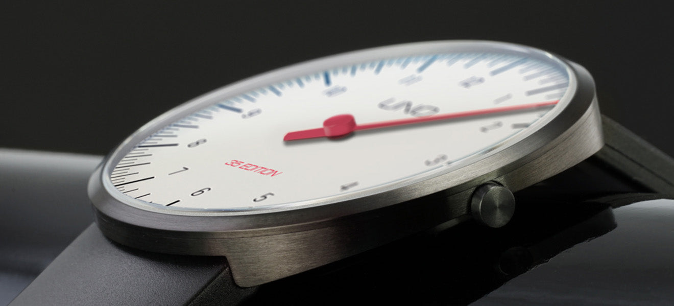 Detailaufnahme der UNO 35 Edition Quarzuhr in Weiß: Das ultraflache Edelstahlgehäuse mit gebürsteter Oberfläche wirkt elegant und modern. Das klare weiße Zifferblatt mit schwarzer Minuterie und der rote Einzelzeiger machen diese Einzeigeruhr zur ikonischen Designuhr. Mit schwarzem Lederarmband und minimalistischem Look steht die Armbanduhr für Ruhe und Präzision. Jetzt diese besondere Uhr mit einem Zeiger exklusiv kaufen oder online bestellen.