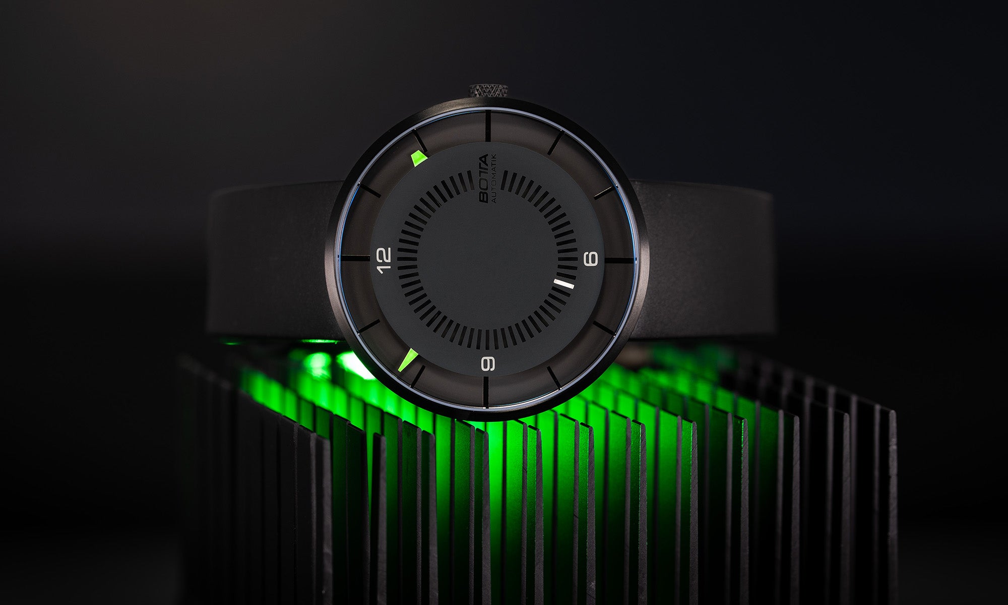 Die BOTTA CLAVIUS Automatik 44 mm erscheint hier als futuristische Designuhr, platziert auf einem schwarz-grünen Kühlkörper, der das avantgardistische Erscheinungsbild verstärkt. Das tiefschwarze Zifferblatt mit konzentrischen Markierungen wird von leuchtend grünen und weißen Indizes akzentuiert. Eine hochwertige Armbanduhr aus Titan mit Automatikwerk und Saphirglas – die perfekte Automatikuhr Designuhr für alle, die eine außergewöhnliche Armbanduhr kaufen oder bestellen möchten.