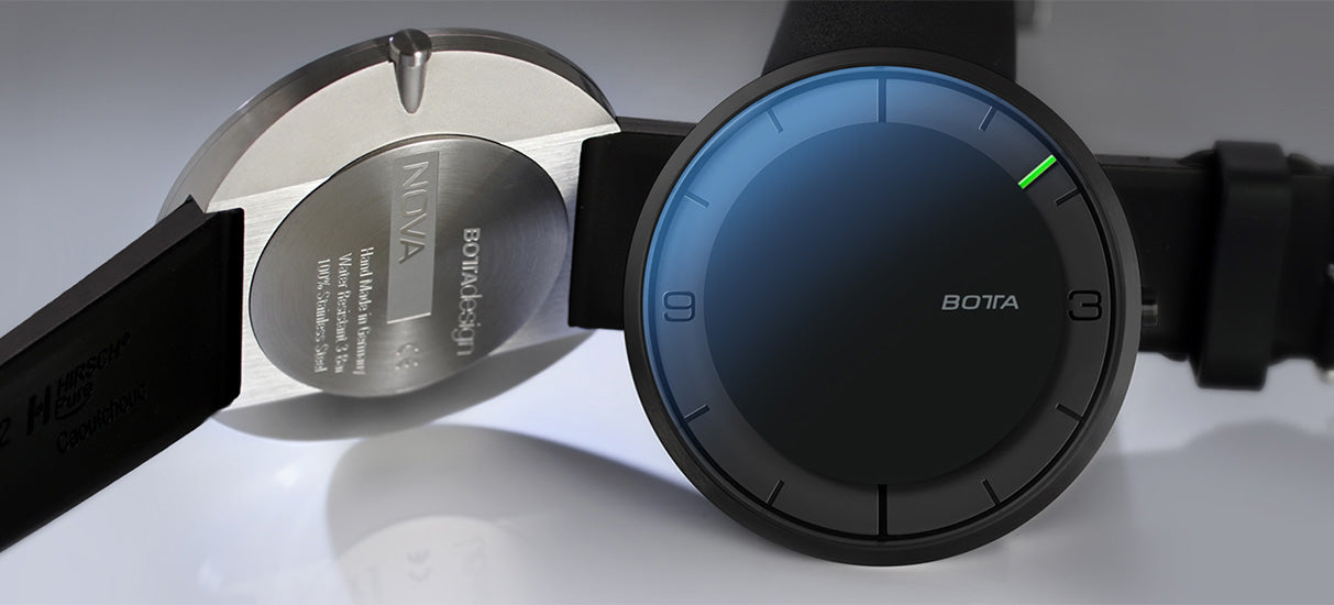 Die BOTTA NOVA Quarzuhr Black Edition in 44 mm zeigt sich als konsequente und flache Designuhr mit puristischem Zifferblatt und nur einem grünen Zeiger. Im Bild sind Vorder- und Rückseite zu sehen: Das minimalistische schwarze Zifferblatt mit markanten Stundenindizes sowie der gravierte Titanboden mit Modell- und Fertigungsangaben. Diese Einzeigeruhr reduziert die Zeit auf das Wesentliche und vermittelt Gelassenheit. Die Armbanduhr kann online als exklusive Uhr mit einem Zeiger gekauft oder bestellt werden.