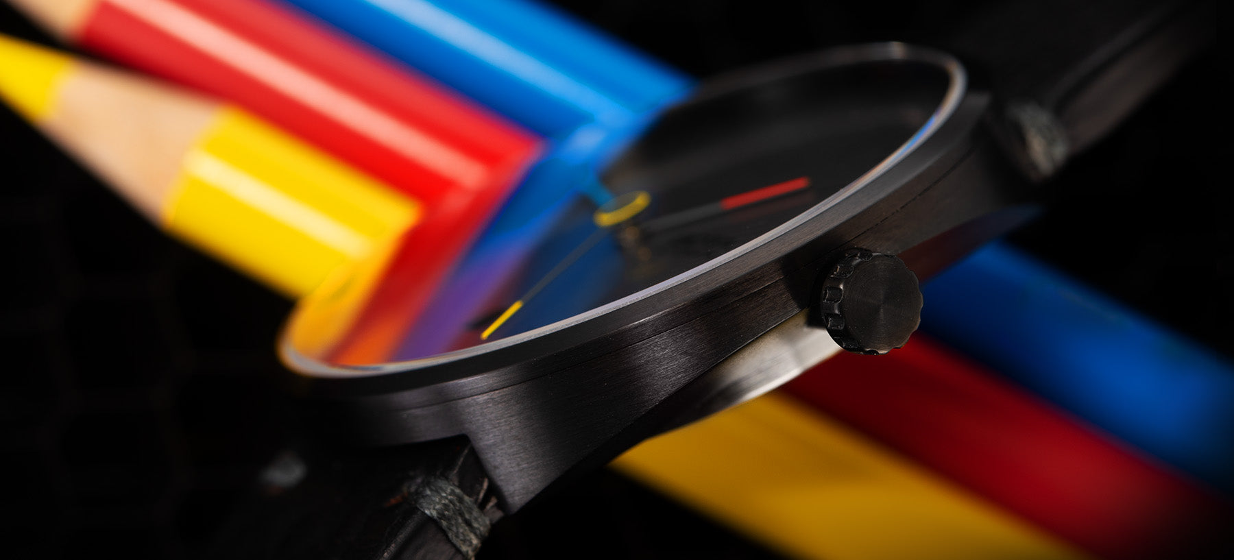 Detailaufnahme der BOTTA TRES colores Automatik: Gezeigt wird das hochwertige, matt gebürstete Gehäuse der Automatikuhr mit seitlicher Krone und gewölbtem Glas. Im Hintergrund liegen farbige Stifte in Blau, Rot und Gelb, die die drei markanten Zeigerfarben der Designuhr widerspiegeln. Diese Armbanduhr ist eine besondere Interpretation, ideal für Designliebhaber, die eine außergewöhnliche Automatikuhr kaufen oder bestellen möchten.