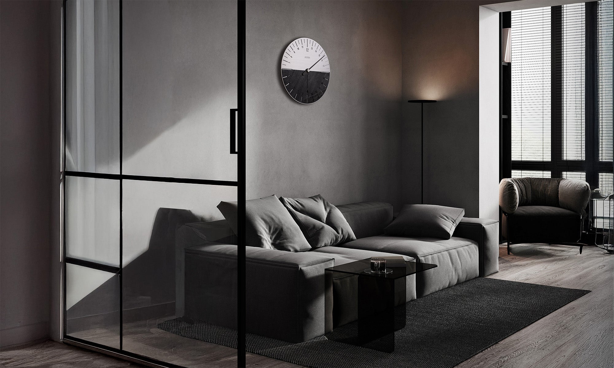 Stilvoll eingerichtetes Wohnzimmer mit modernem, minimalistischen Interieur in Grautönen. An der Wand hängt die UNO 24 Slate Wanduhr von BOTTA, eine 24 Stunden Designwanduhr mit einem Zeiger. Das Zifferblatt ist halb aus gebürstetem Edelstahl, halb aus natürlichem Schiefer gefertigt und verleiht dem Raum ein architektonisches Statement. Diese Wanduhr mit Schiefer vereint Funktionalität und Design – jetzt exklusiv UNO 24 Wanduhr kaufen oder bestellen