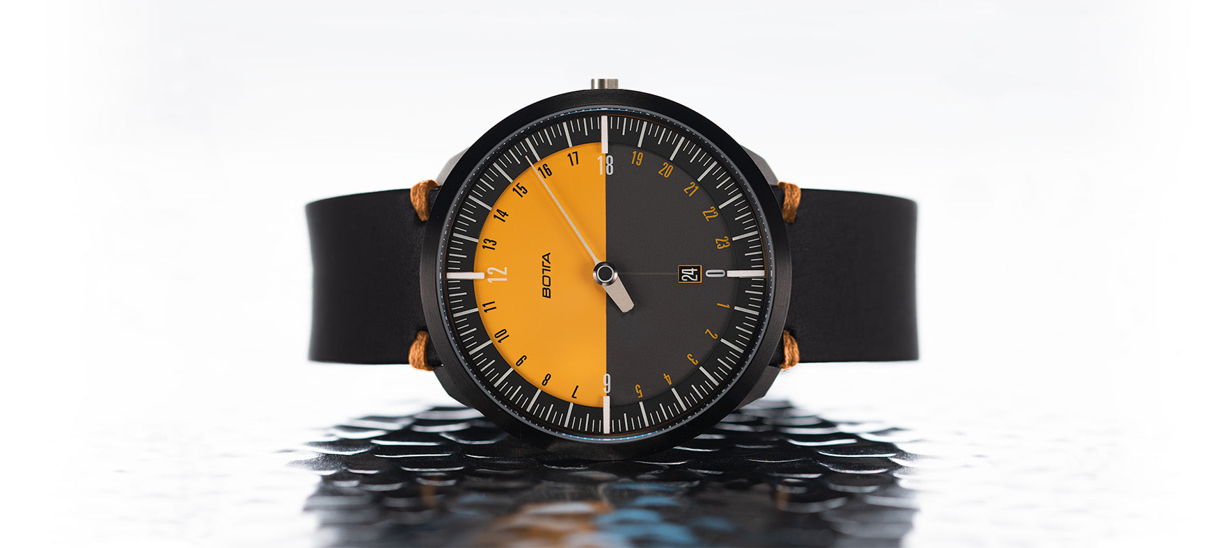 Die BOTTA UNO 24 Jubiläumsedition Quarzuhr mit 45 mm Titangehäuse in der Frontansicht. Das markante 24-Stunden-Zifferblatt ist in zwei Hälften geteilt – die obere Hälfte in kräftigem Orange für den Tag, die untere in Schwarz für die Nacht. Ein einzelner Zeiger zeigt die Zeit auf einen Blick, ergänzt durch eine Datumsanzeige bei 6 Uhr. Mit schwarzem Lederarmband und klarer Linienführung ist diese Einzeigeruhr eine preisgekrönte Designuhr – jetzt kaufen oder bestellen für Liebhaber puristischer Armbanduhren.