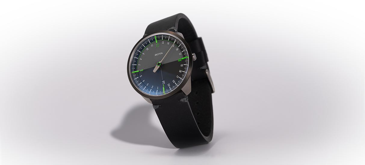 Die BOTTA UNO 24 Quarzuhr in der 40 mm Version wird hier in einer schrägen Ansicht präsentiert. Das minimalistische Zifferblatt zeigt den vollen 24-Stunden-Tag mit einem einzigen Zeiger, der über eine klare Skala läuft. Grüne Akzente bei den Hauptstundenmarken verleihen der Designuhr Frische und Modernität. Das schwarze Lederarmband unterstreicht die Eleganz dieser Einzeigeruhr. Eine außergewöhnliche Armbanduhr für Menschen, die bewusst Zeit erleben – jetzt bestellen oder kaufen.