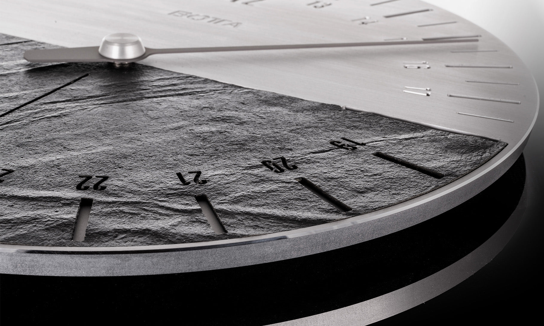 Detailaufnahme der UNO 24 Slate Wanduhr im Schieferdesign: Das Bild zeigt das Zifferblatt mit markanter Natursteinstruktur, die durch lasergravierte Markierungen und gefräste Zahlen veredelt ist. Als Designwanduhr mit 24-Stunden-Anzeige bewegt sich nur ein Zeiger im Tagesrhythmus – die obere Hälfte für Tag, die untere für Nacht. Eine wertige Wanduhr mit Schiefer, gefertigt in Deutschland, die Gelassenheit und bewusstes Leben symbolisiert. Jetzt kaufen oder bestellen