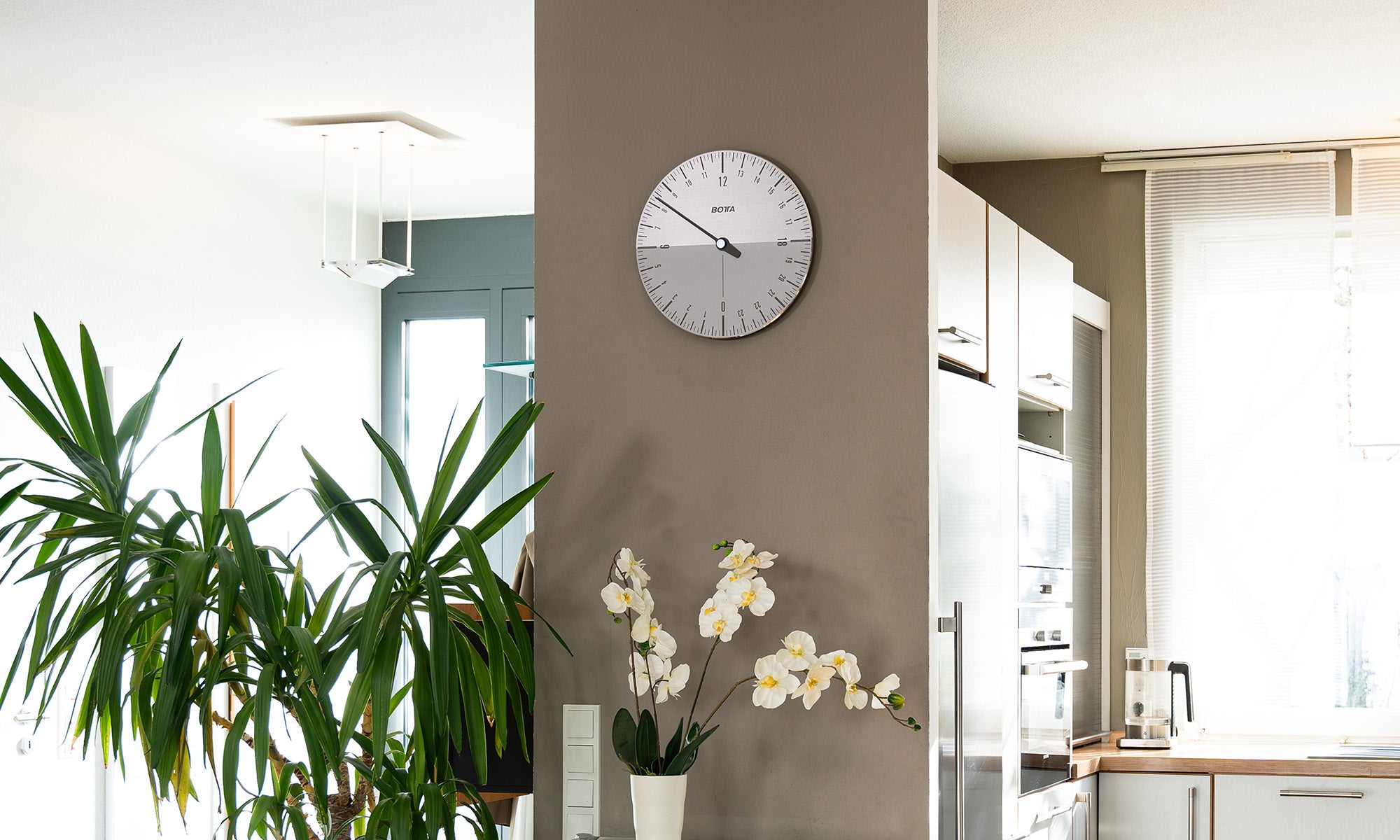 Das Bild zeigt die BOTTA UNO 24 Wanduhr, eine hochwertige Designwanduhr aus massivem Aluminium. Das gebürstete, silberne Zifferblatt ist in 24 Stunden eingeteilt, wobei die obere Hälfte den Tag und die untere Hälfte die Nacht symbolisiert. Ein einziger markanter Zeiger bewegt sich synchron zum Sonnenlauf und umrundet das Zifferblatt nur einmal pro Tag – das Prinzip der 24h Einzeigeruhr. Diese außergewöhnliche Wanduhr vereint modernes Design, deutsche Handarbeit und eine völlig neue Art der Zeitdarstellung.