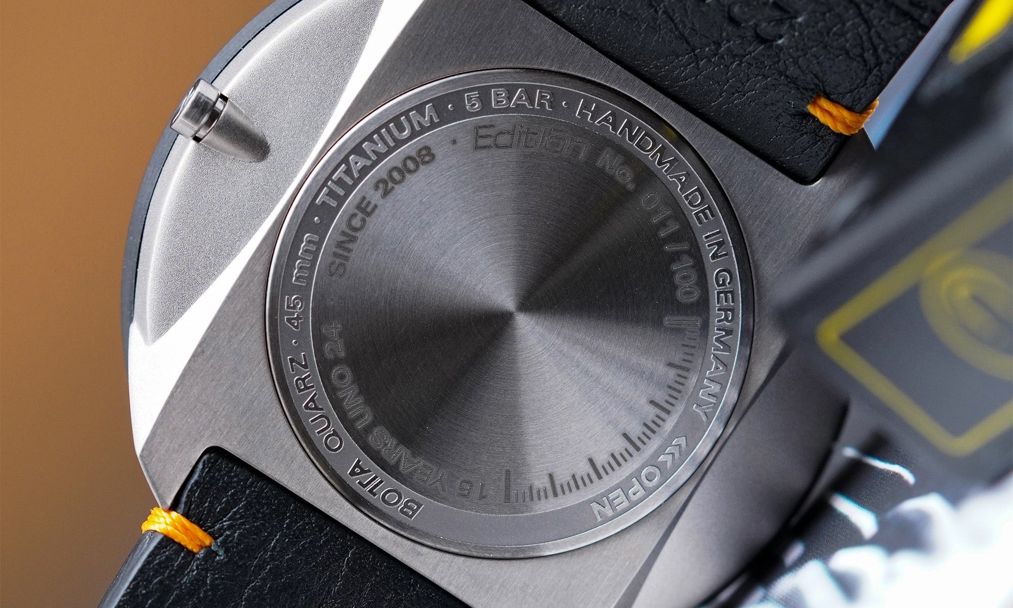 Detailaufnahme des Gehäusebodens der BOTTA UNO 24 Jubiläumsedition Quarzuhr. Sichtbar ist die feine Gravur auf dem gebürsteten Titanboden mit Angaben wie „45 mm“, „Titanium“, „5 BAR“, „Handmade in Germany“ sowie die Limitierungsnummer „Edition No. 011/100“. Die präzise Verarbeitung, das robuste Material und die handwerkliche Qualität machen diese preisgekrönte Designuhr zur exklusiven Einzeigeruhr – jetzt kaufen oder bestellen.